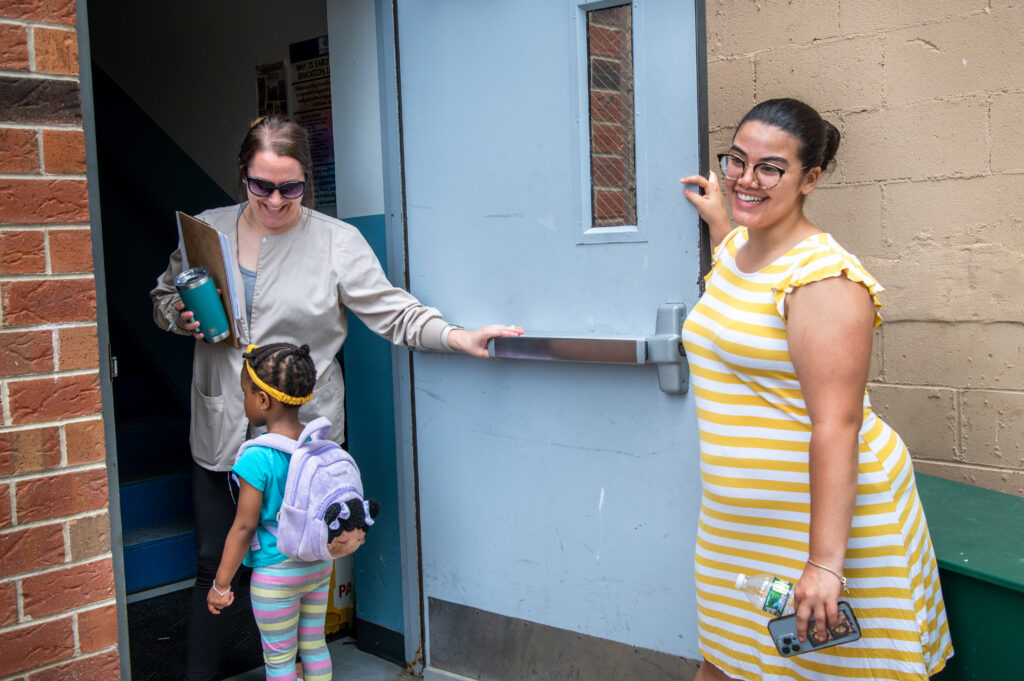 An educator holding the door open for a child. 