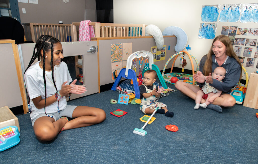 Two educator sitting with two young children clapping hands.