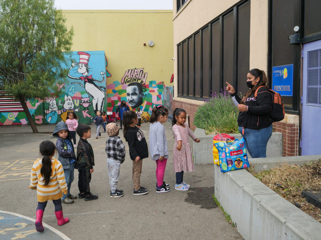 Children lined up to enter a classroom. The educator is leading the children at the top of the line.