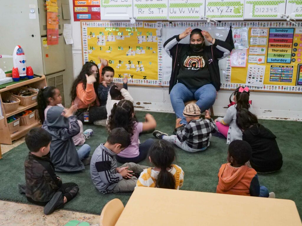 An educator at the front of a classroom instructing children. 