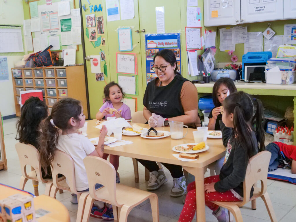 An educator gathered around the table with young children. 